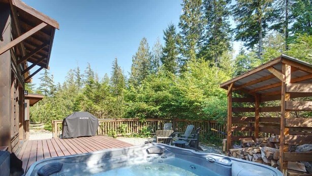 A hot tub on a wooden deck with outdoor furniture, surrounded by trees and a wooden fence. - A slice of paradise with Hot Tub - Pet Friendly (Port Renfrew)