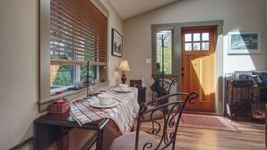 A dining area with a table set for two, a chair, a lamp, and a window with blinds.