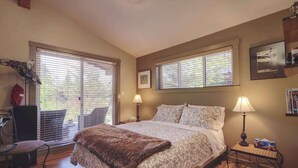 A bedroom with a large bed, two bedside lamps, a chair, and a window with blinds.