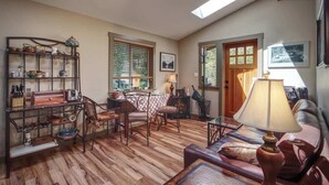 A cozy living room with a wooden floor, a dining area with a table and chairs, and a bookshelf filled with various items.