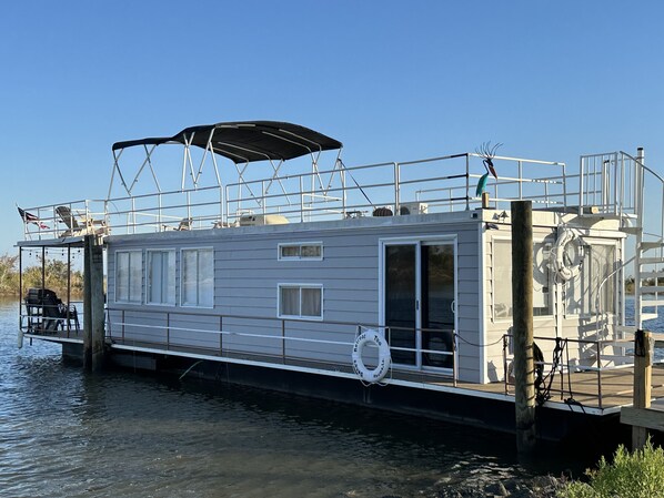 Een stilstaande woonboot met een overdekt dek, ramen en een reddingsboei.