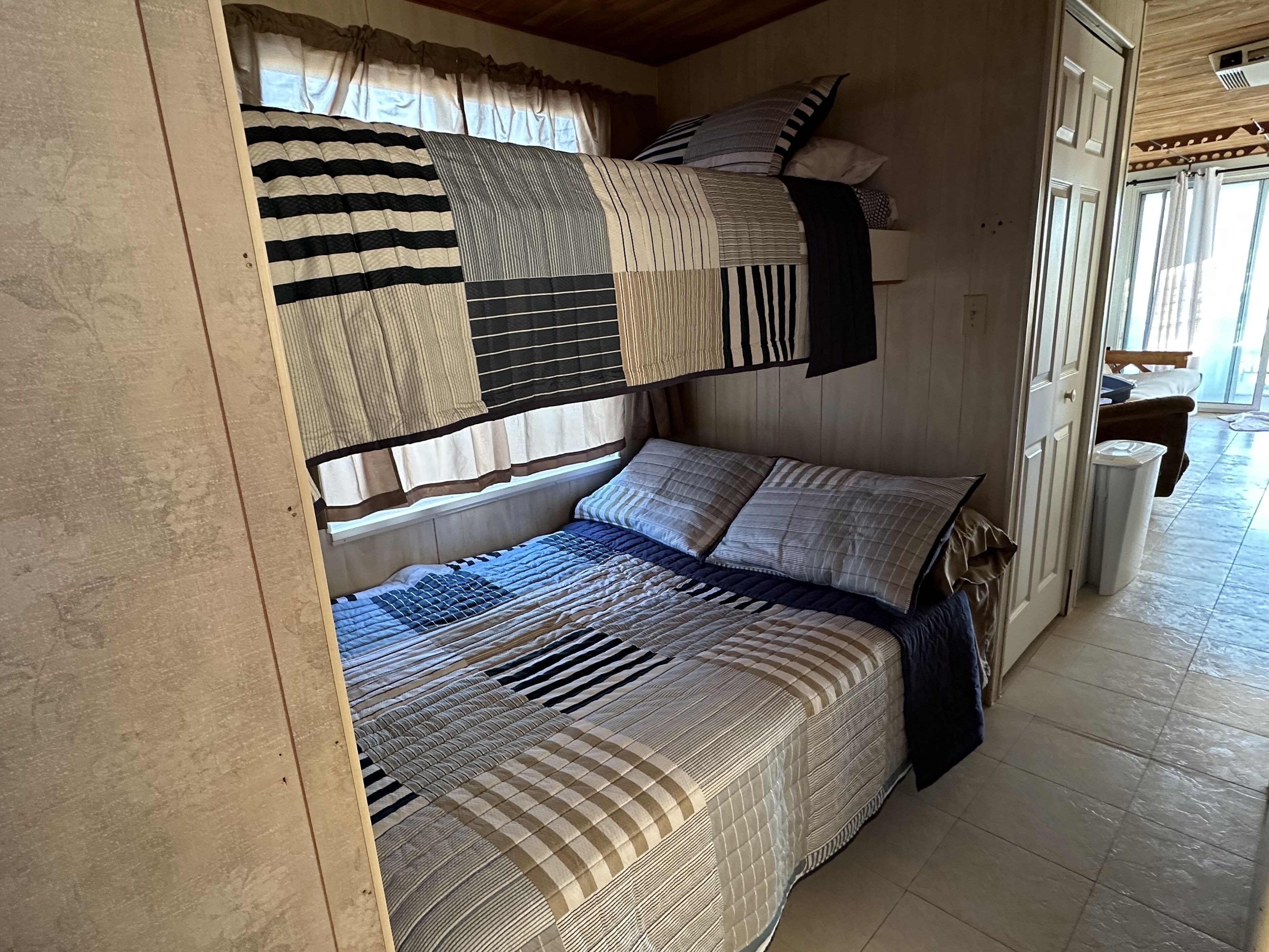 A bunk bed room with a window, curtains, and a door.