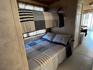 Een slaapkamer met stapelbed, raam, gordijnen en een deur.