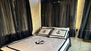 A neatly made bed with a striped bedspread and pillows featuring anchor designs, set against a backdrop of dark curtains and a wooden ceiling. - Awesome retreat on the water with sunrise (Chauvin)