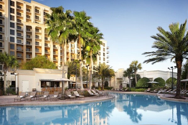 A hotel with a swimming pool, palm trees, and lounge chairs.