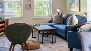 A living room with a blue sofa, a green armchair, a wooden coffee table, and a lamp. - Skyline Views, Park For Free and Walk To Downtown, PPG, Convention Center (Pittsburgh)