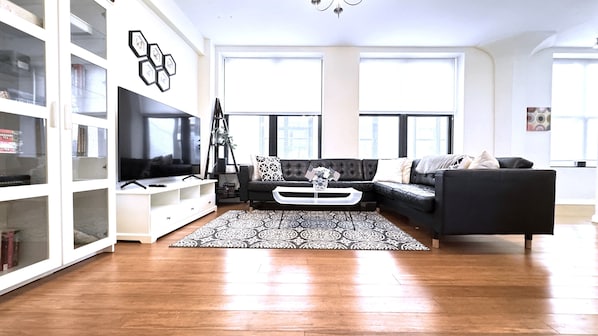 A living room with a black sofa, white entertainment unit, and a patterned rug.