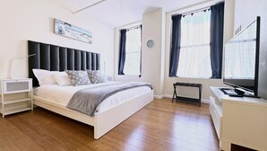 A modern bedroom with a bed, bedside table, and a desk with a computer. - Spacious Sunlit 3BR • Center of Downtown Boston • Family Favorite (Boston)