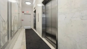 A hallway with marble walls, two elevators, and a black carpet. - Spacious Sunlit 3BR • Center of Downtown Boston • Family Favorite (Boston)