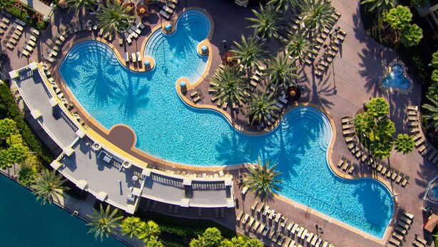 An aerial view of a resort with a large, winding pool surrounded by palm trees and sun loungers. - Orlando | Couples Resort Pad | Pool + Hot Tub (Orlando)