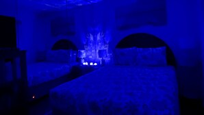 A dimly lit room with a bed, two wall-mounted lamps, and a ceiling with a textured design.