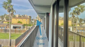 A balcony with a view of the beach, a wooden fence, and a row of blue chairs.