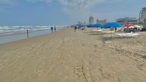 A beach with umbrellas and beach chairs, a sandy shore, and a cityscape in the background.
