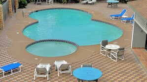 A pool area with lounge chairs, a table, and a tiled deck.