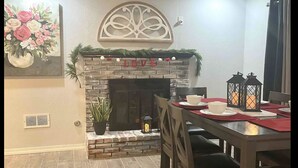 A dining area with a fireplace, a table set with plates and bowls, and a decorative wall piece above the fireplace. - Modern Open House w POOL, close to Fort Bliss (El Paso)