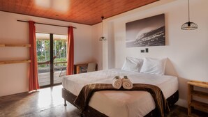 Un dormitorio con una cama grande, techo de madera, vista a través de un ventanal y un cuadro en la pared.