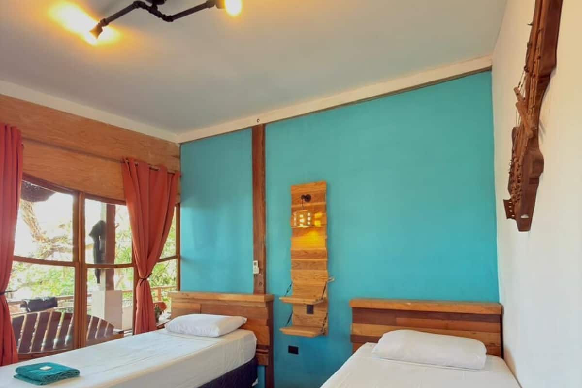 Habitación con dos camas, cabeceros de madera, una repisa con un reloj y una ventana con cortinas.