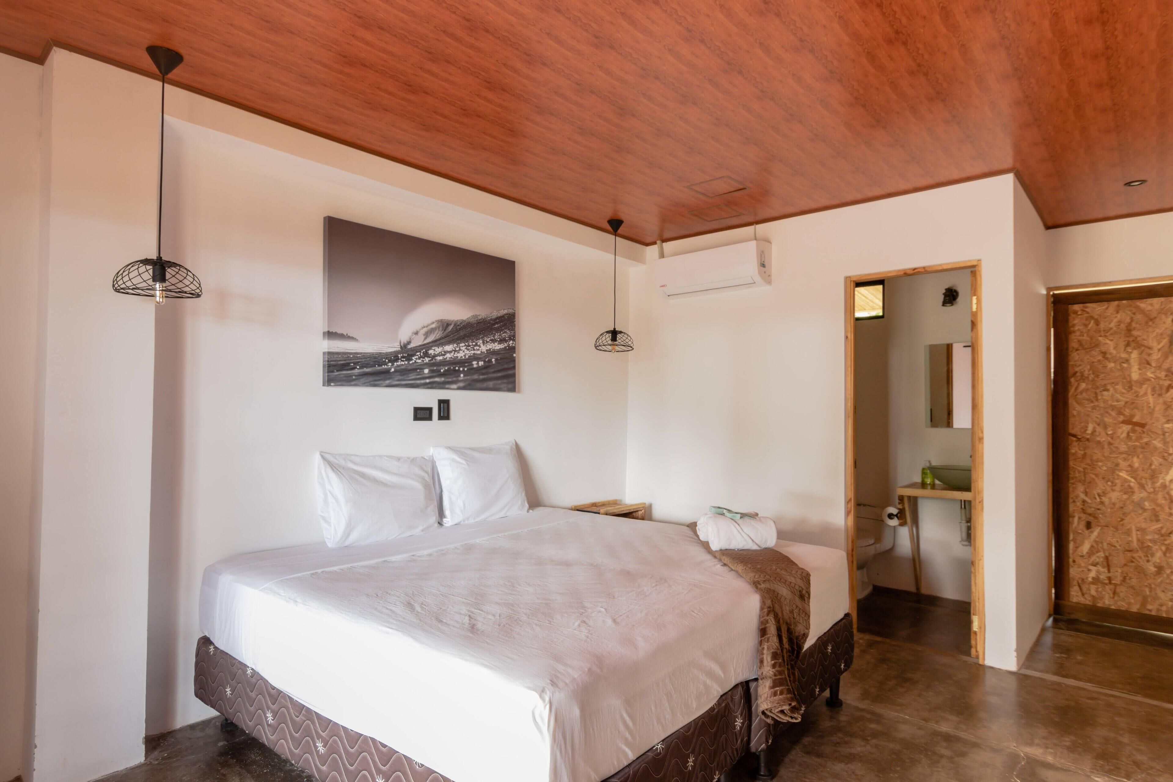 A bedroom with a bed, a wall-mounted air conditioner, and a wooden ceiling.