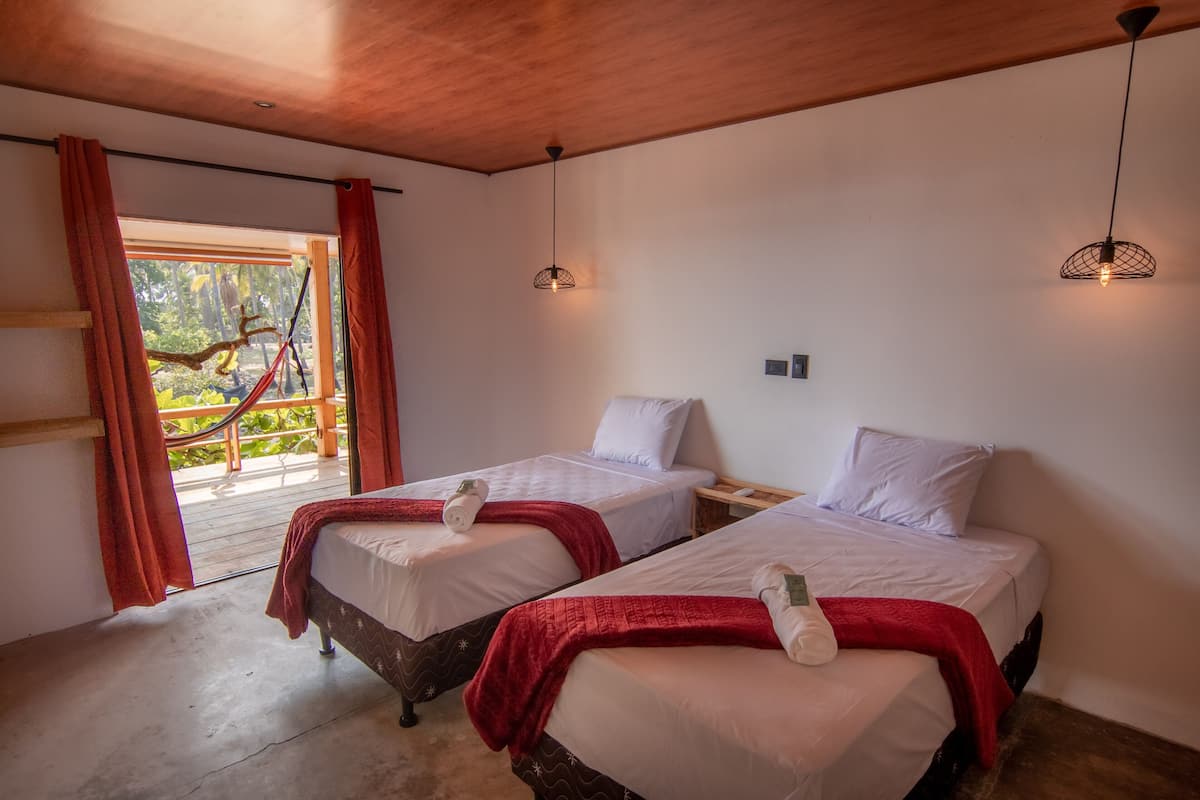 Una habitación con dos camas, techo de madera y una hamaca al lado de la ventana.