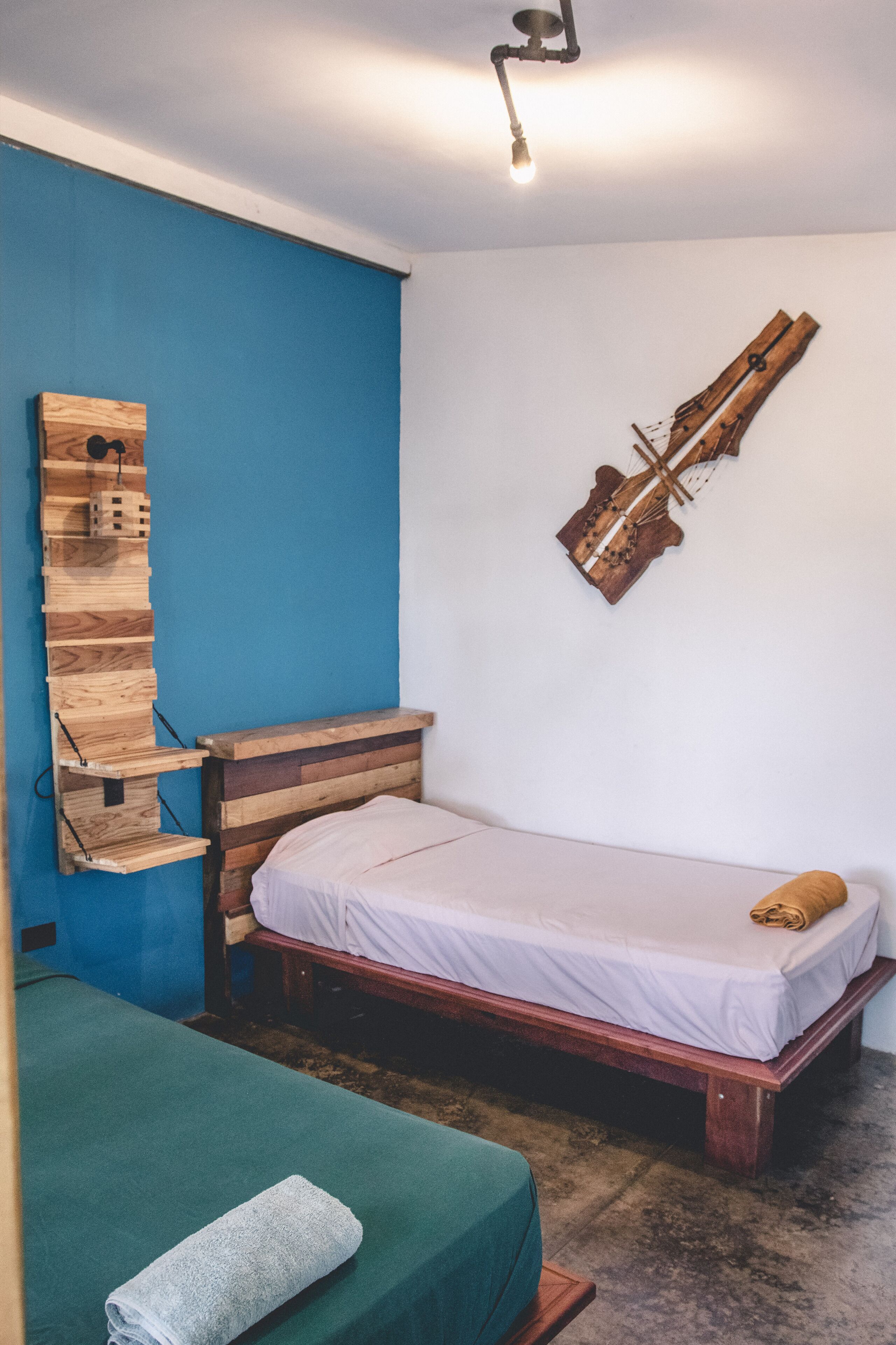 A small, cozy room with a single bed, a wooden headboard, a blue wall, and a unique wooden art piece.