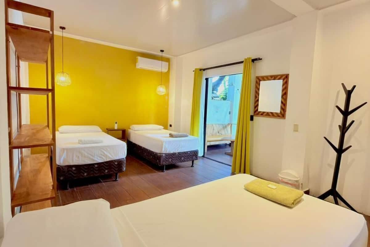 Habitación de hotel con dos camas, piso de madera, pared amarilla y vistas al exterior.