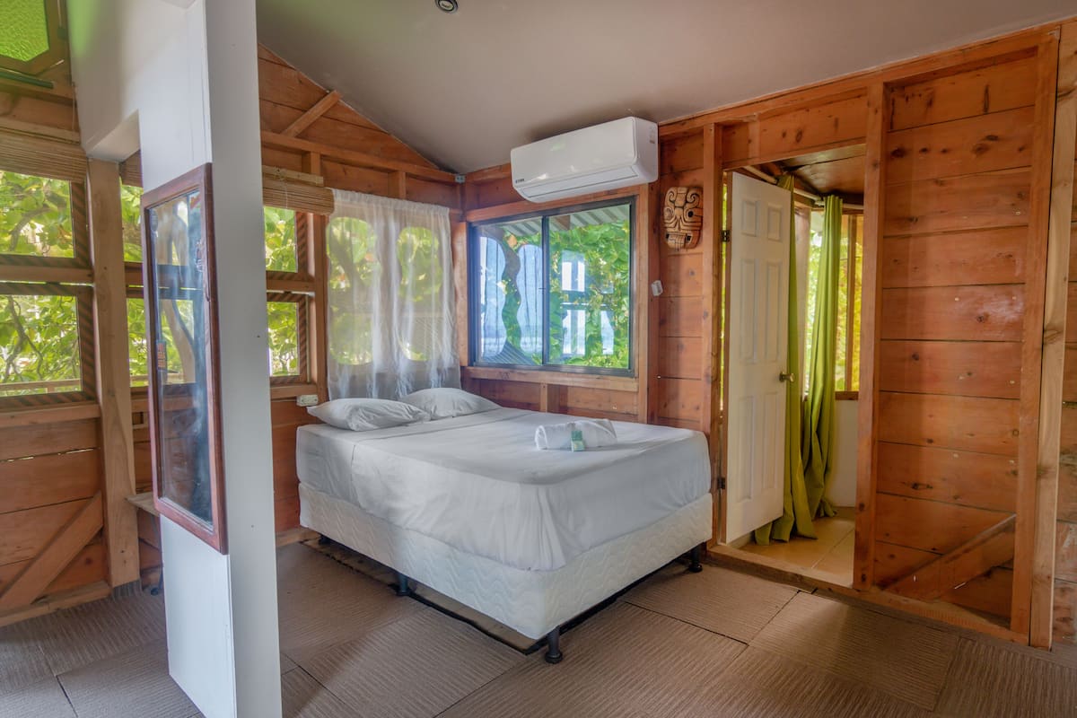 Una habitación de madera con una cama, una ventana y un equipo de aire acondicionado.