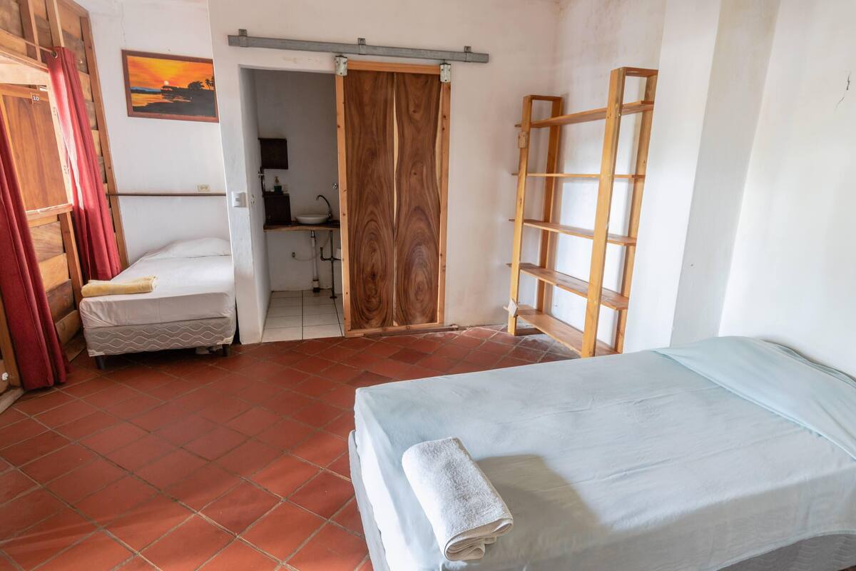 Una habitación con una cama, un escritorio, una silla, un armario y una puerta que da a otra habitación.