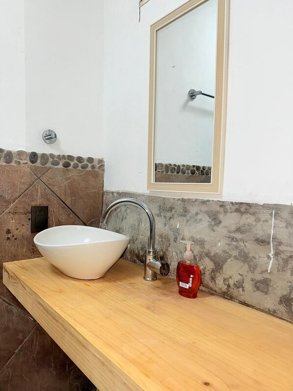 A bathroom with a white vessel sink, a wooden countertop, a mirror, and a red soap dispenser.