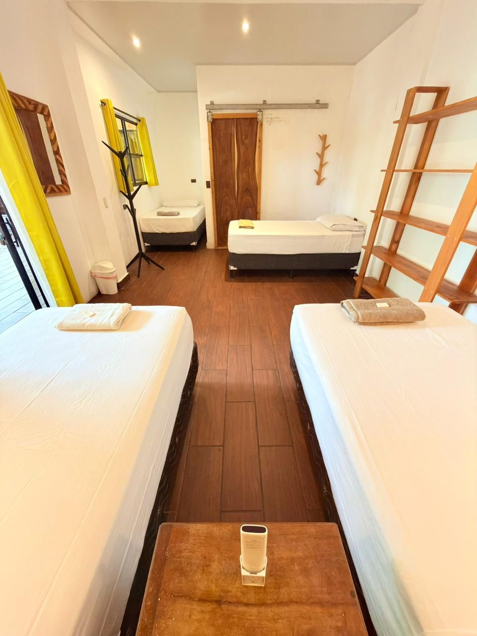 Habitación de hotel con dos camas, piso de madera, una mesita con un vaso y una escalera de madera.