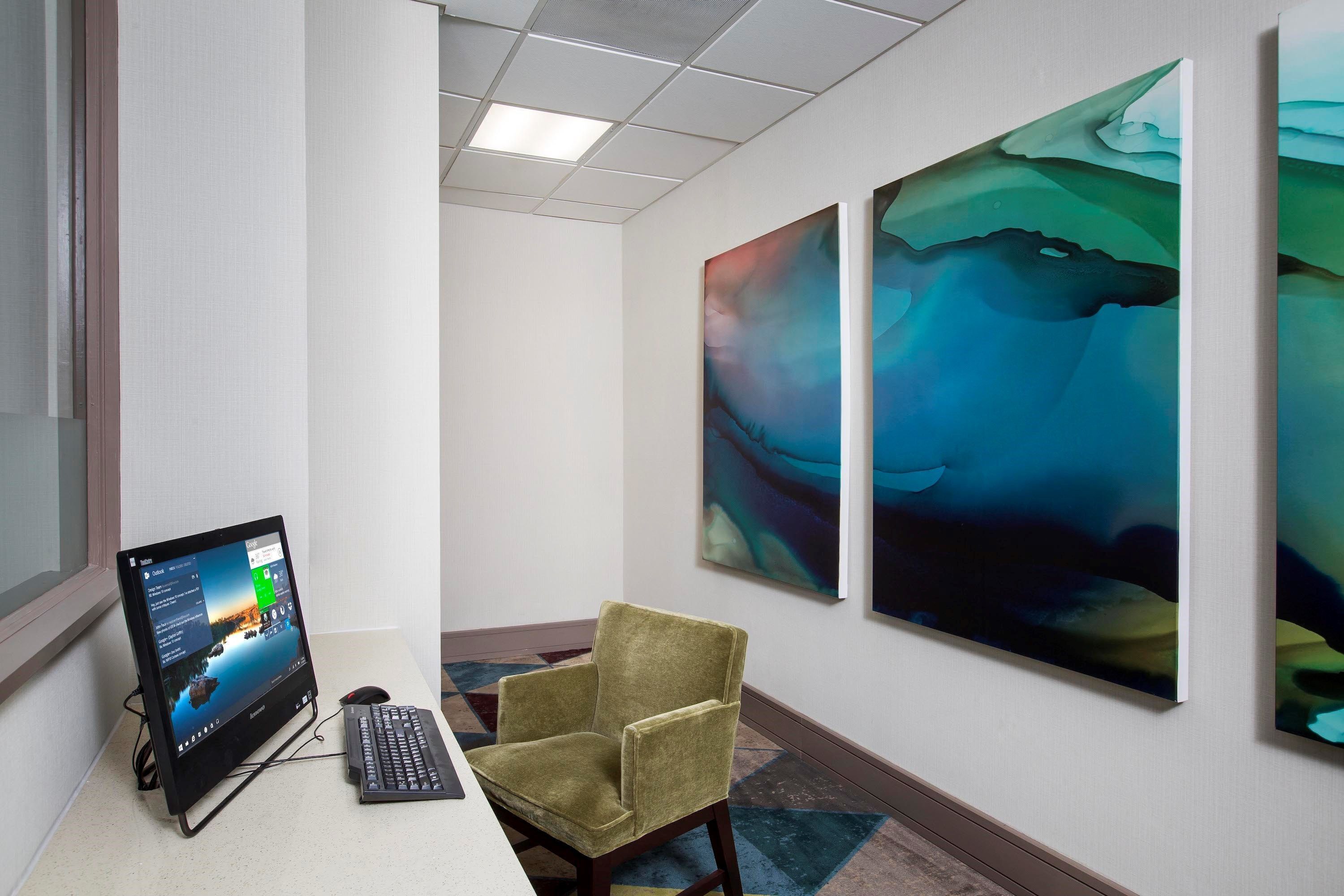 Un espacio de oficina moderno con un ordenador de escritorio, una silla verde y arte abstracto en la pared.