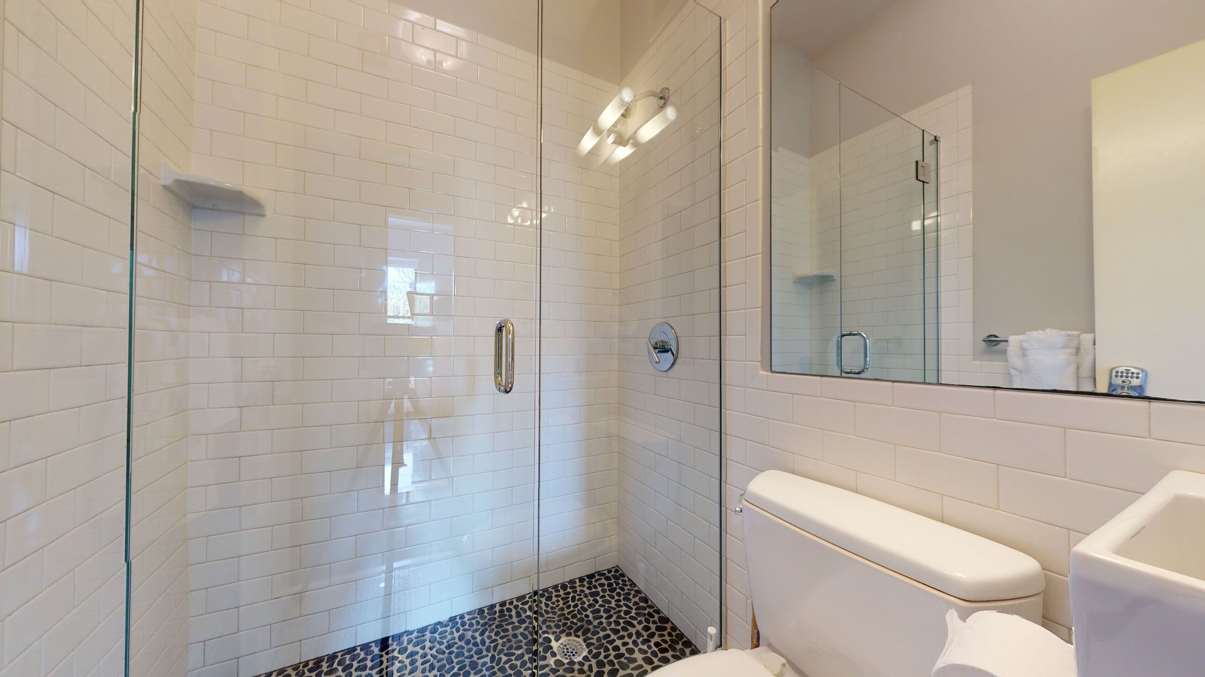 Et moderne badeværelse med hvide metrofliser, en brusekabine i glas, et toilet og et spejl.