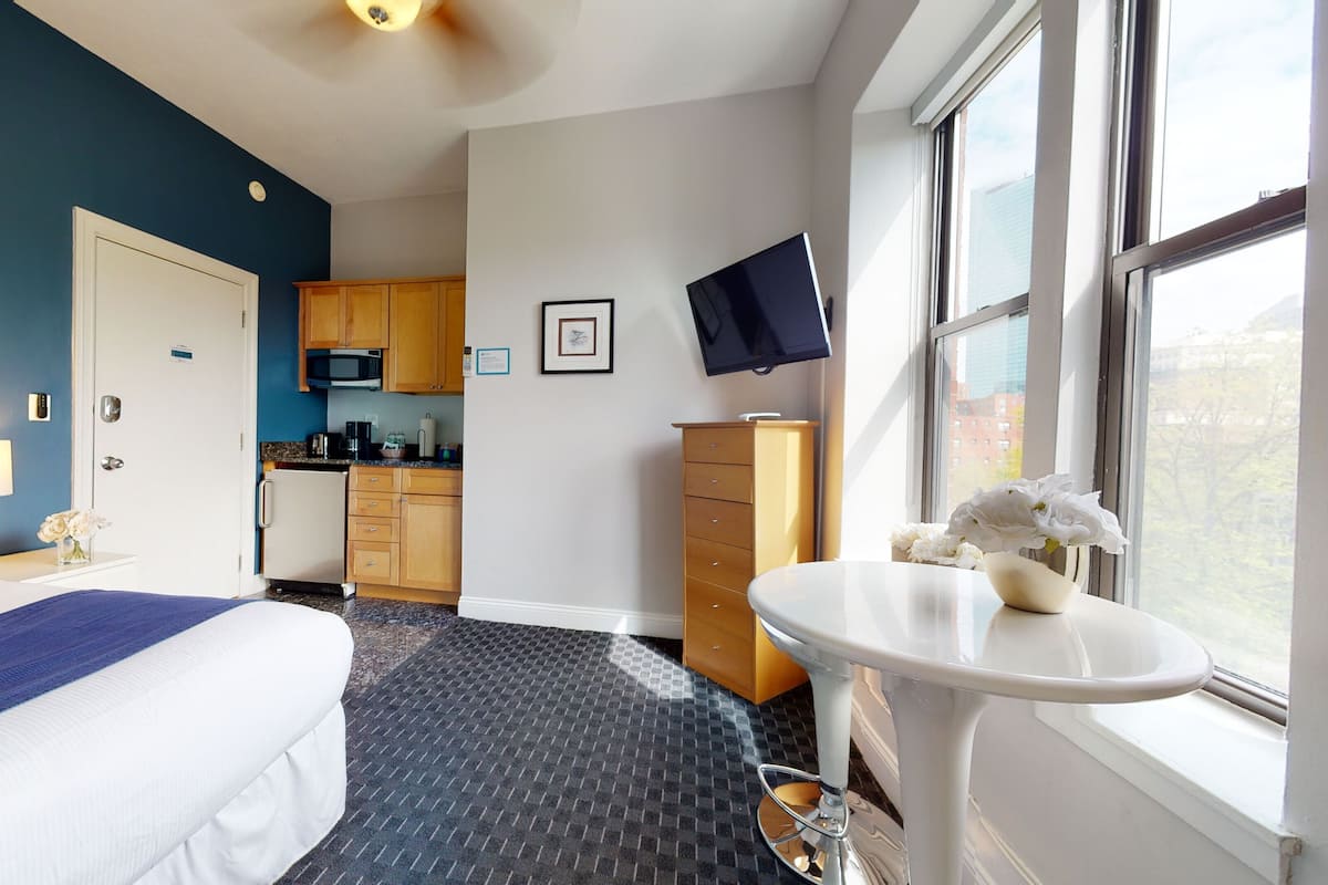 Habitación de hotel con cama, una mesita con flores, televisión, microondas y zona de cocina.