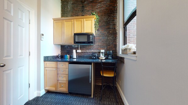 A compact kitchen with wooden cabinets, a built-in microwave, a small refrigerator, and a window with a view.