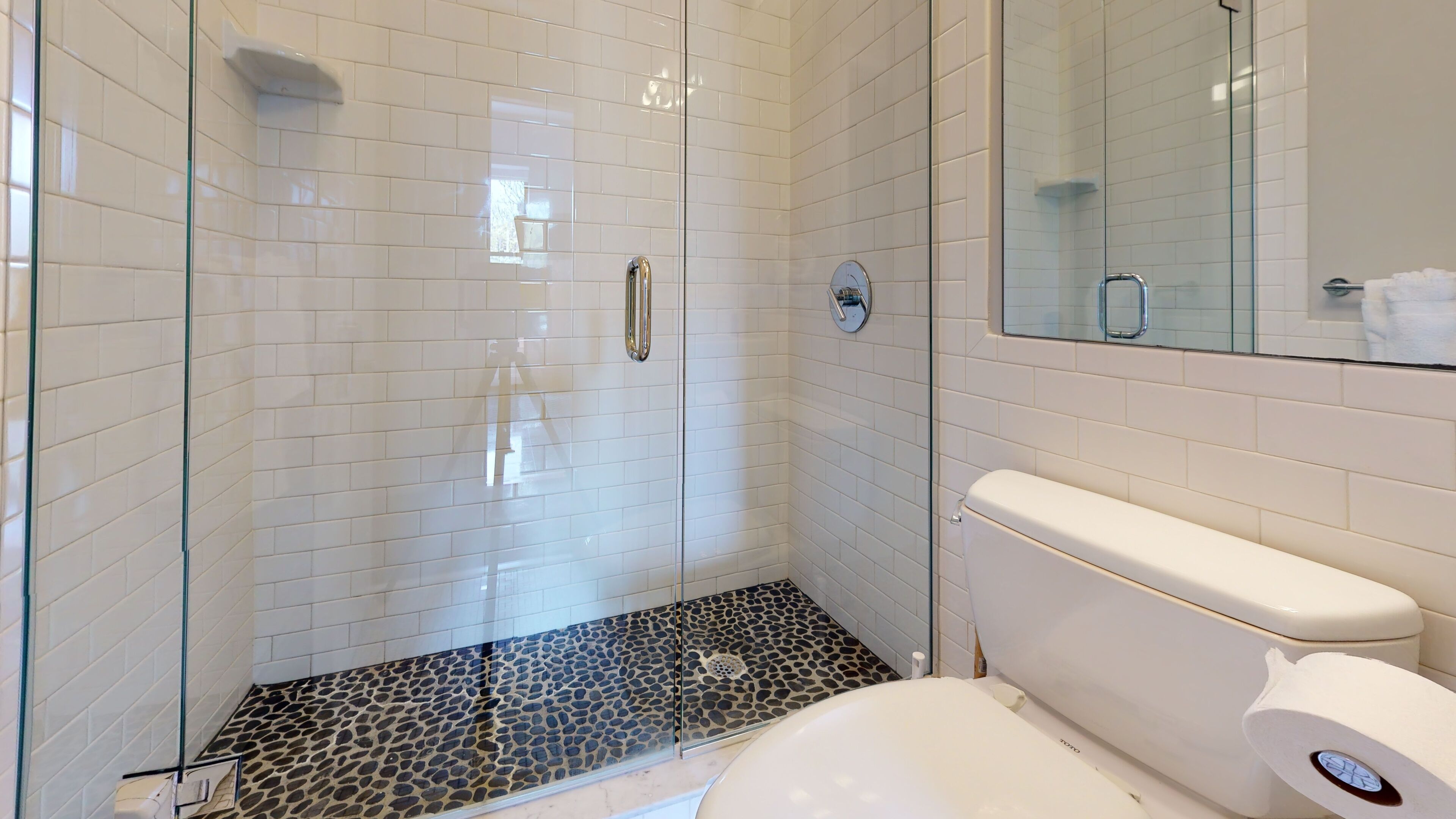 A modern bathroom with white subway tiles, a glass shower enclosure, a white toilet, and a marble-patterned shower floor.