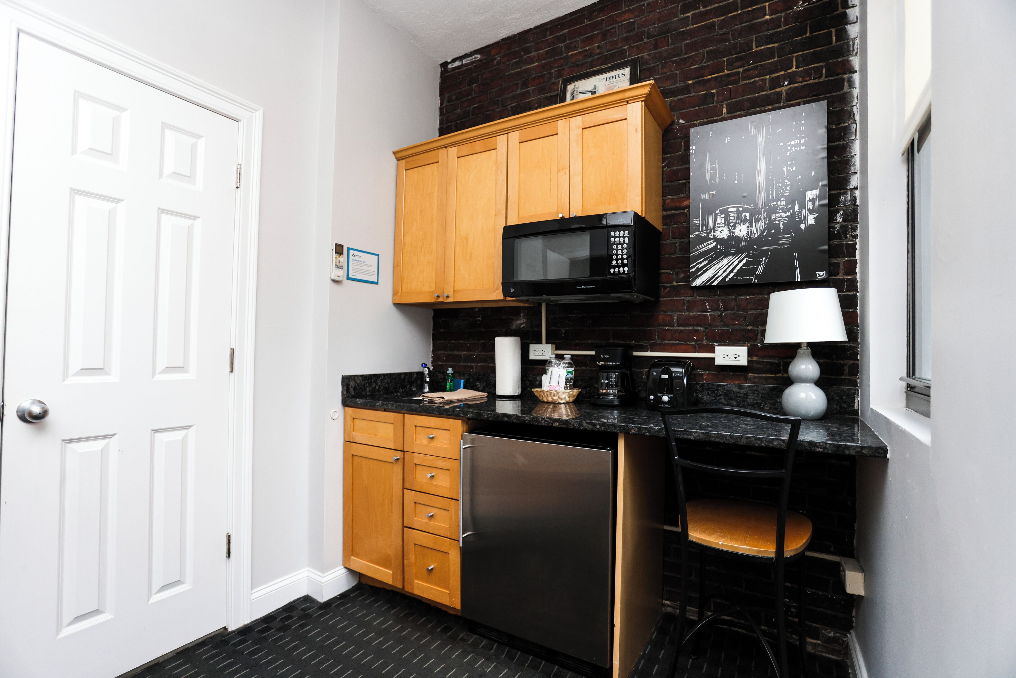 A compact kitchen with wooden cabinets, a stainless steel refrigerator, a microwave, and a black countertop.