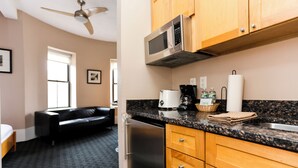 A compact kitchen with wooden cabinets, a stainless steel microwave, a coffee maker, and a refrigerator. - Maverick Suites at 400 Columbus Ave (Boston)
