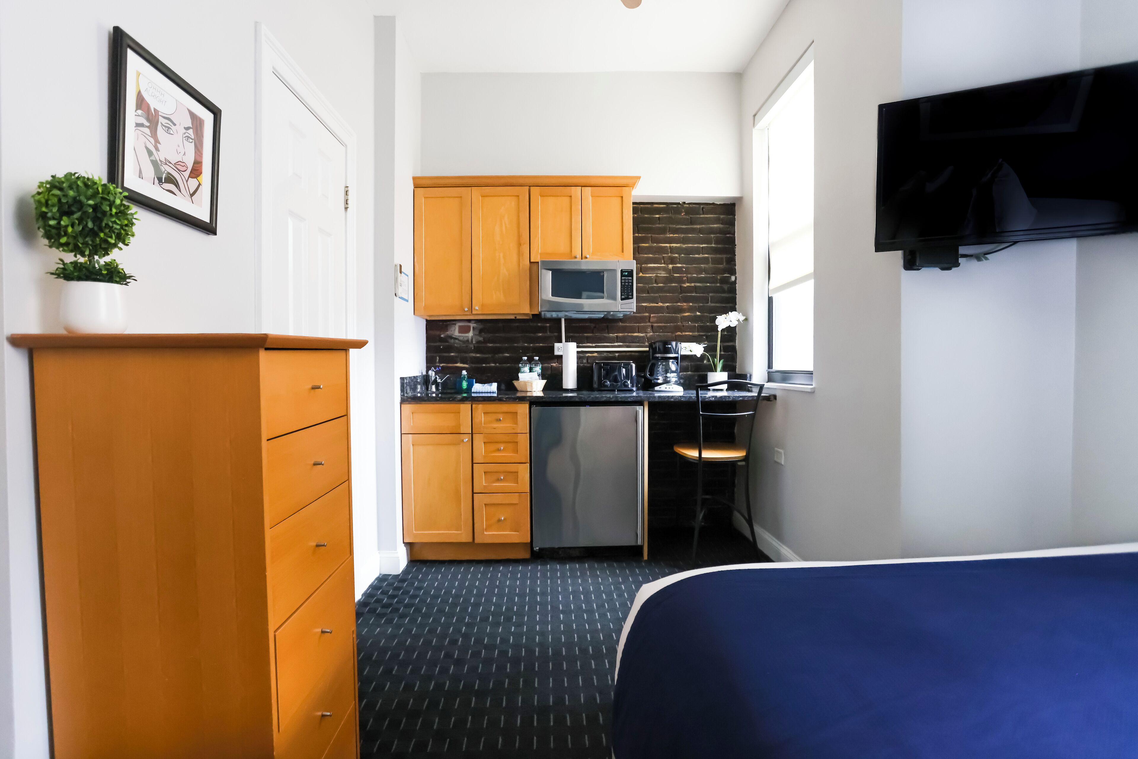 Een compacte hotelkamer met kitchenette, een bed, een televisie en een kleine bloempot.