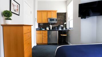 Een compacte hotelkamer met kitchenette, een bed, een televisie en een kleine bloempot.