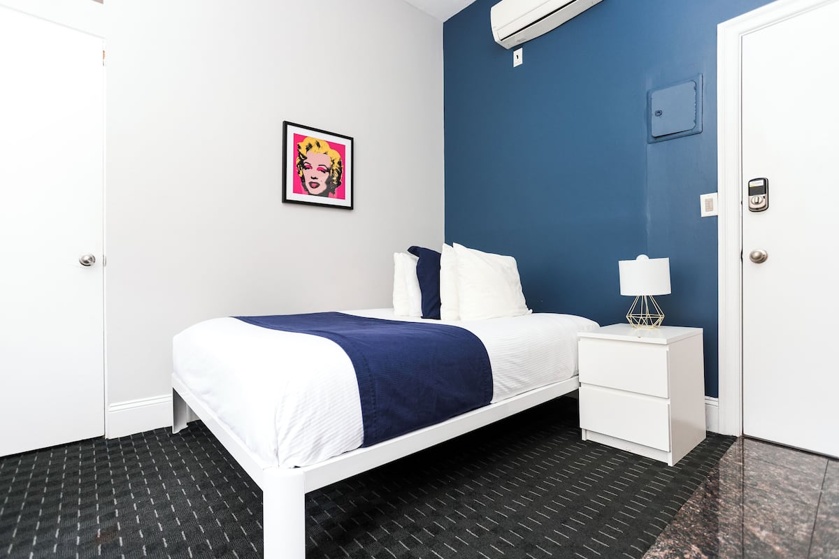 Habitación de hotel con cama, mesita de noche, cuadro enmarcado en la pared y una puerta.