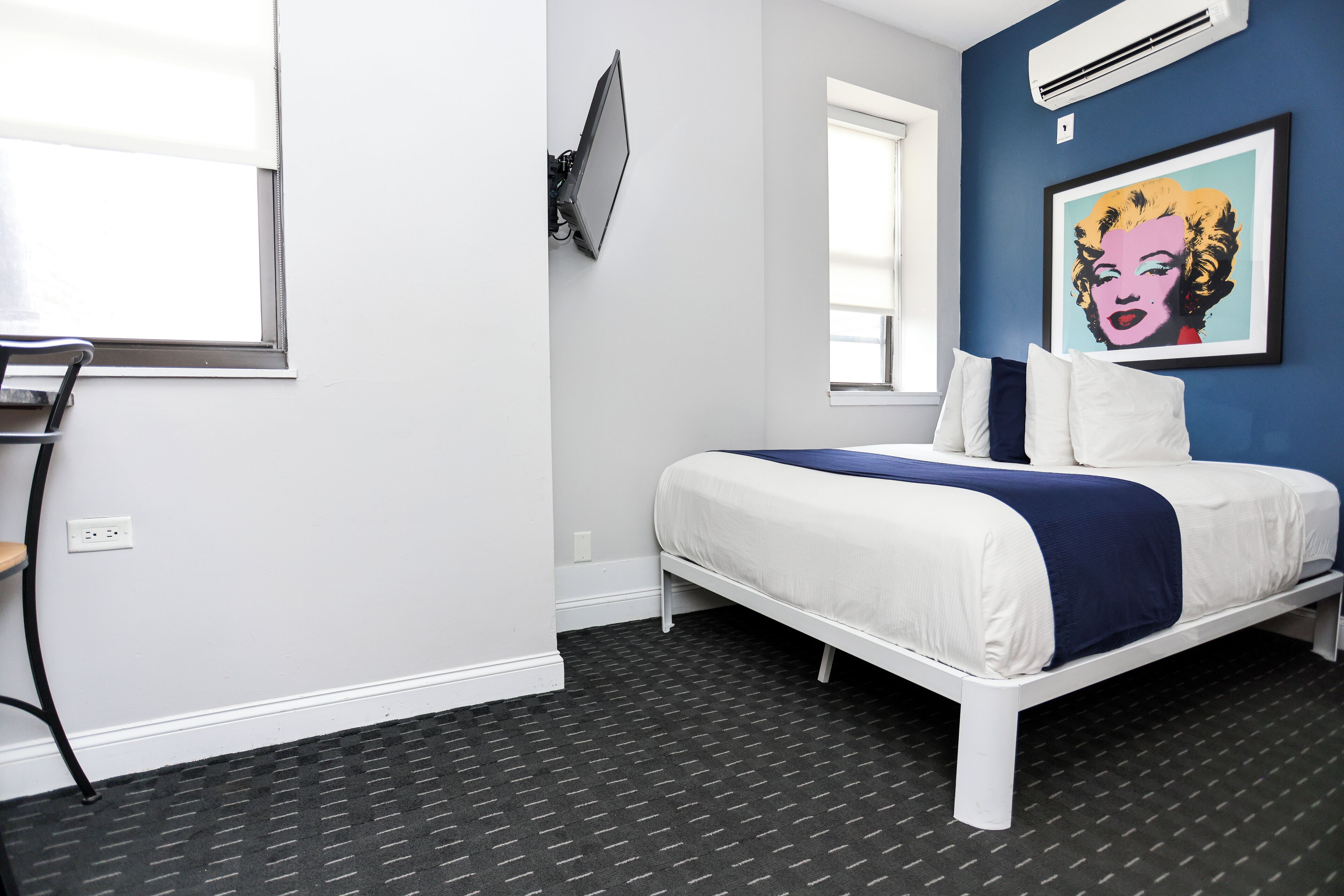 A bedroom with a bed, a TV mounted on the wall, an air conditioner, and a window.