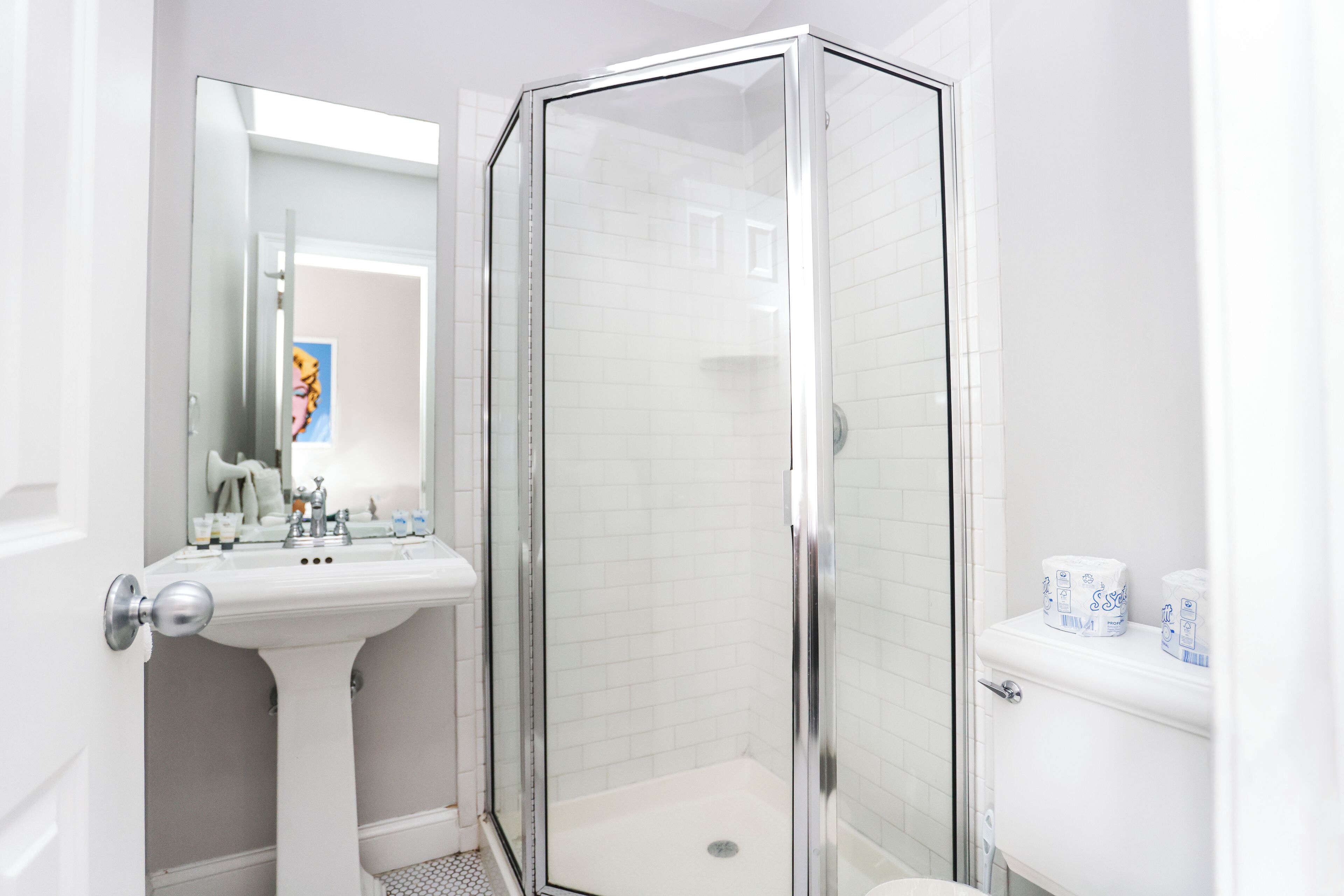 Une salle de bain moderne avec une douche à parois de verre, un lavabo sur colonne et des toilettes avec du papier toilette.