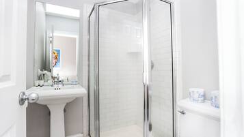 Une salle de bain moderne avec une douche à parois de verre, un lavabo sur colonne et des toilettes avec du papier toilette.