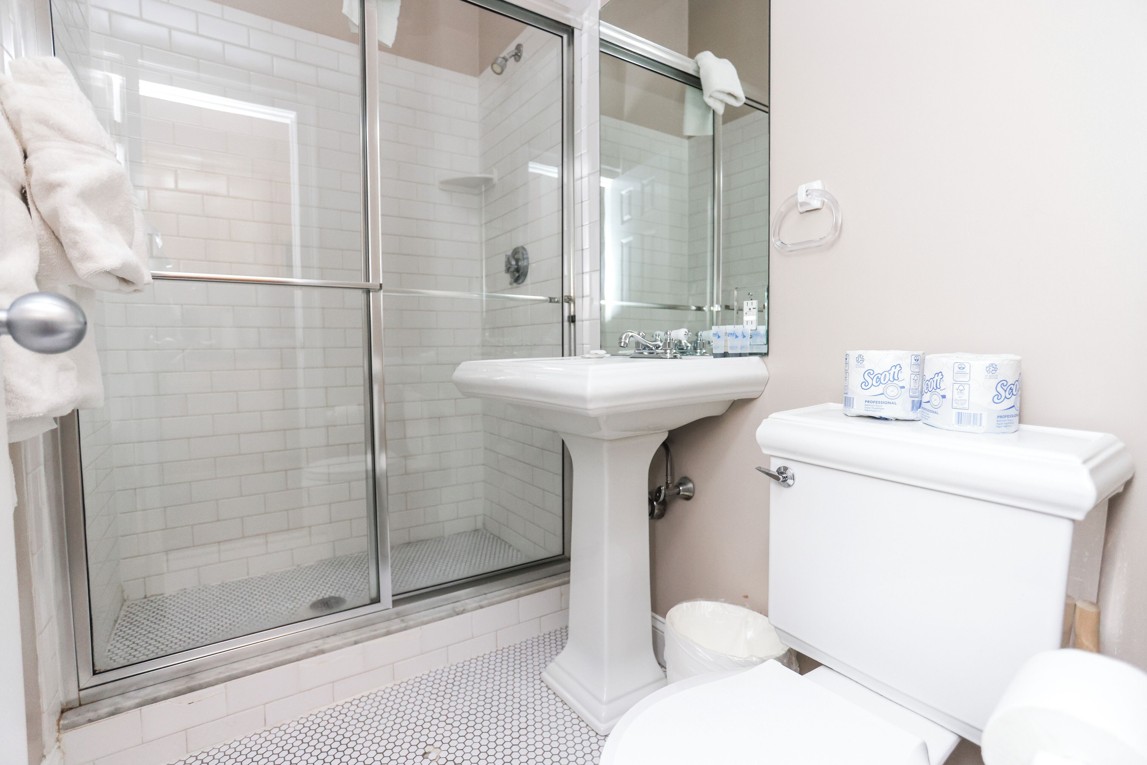 A bathroom with a glass shower enclosure, a pedestal sink, and a toilet.
