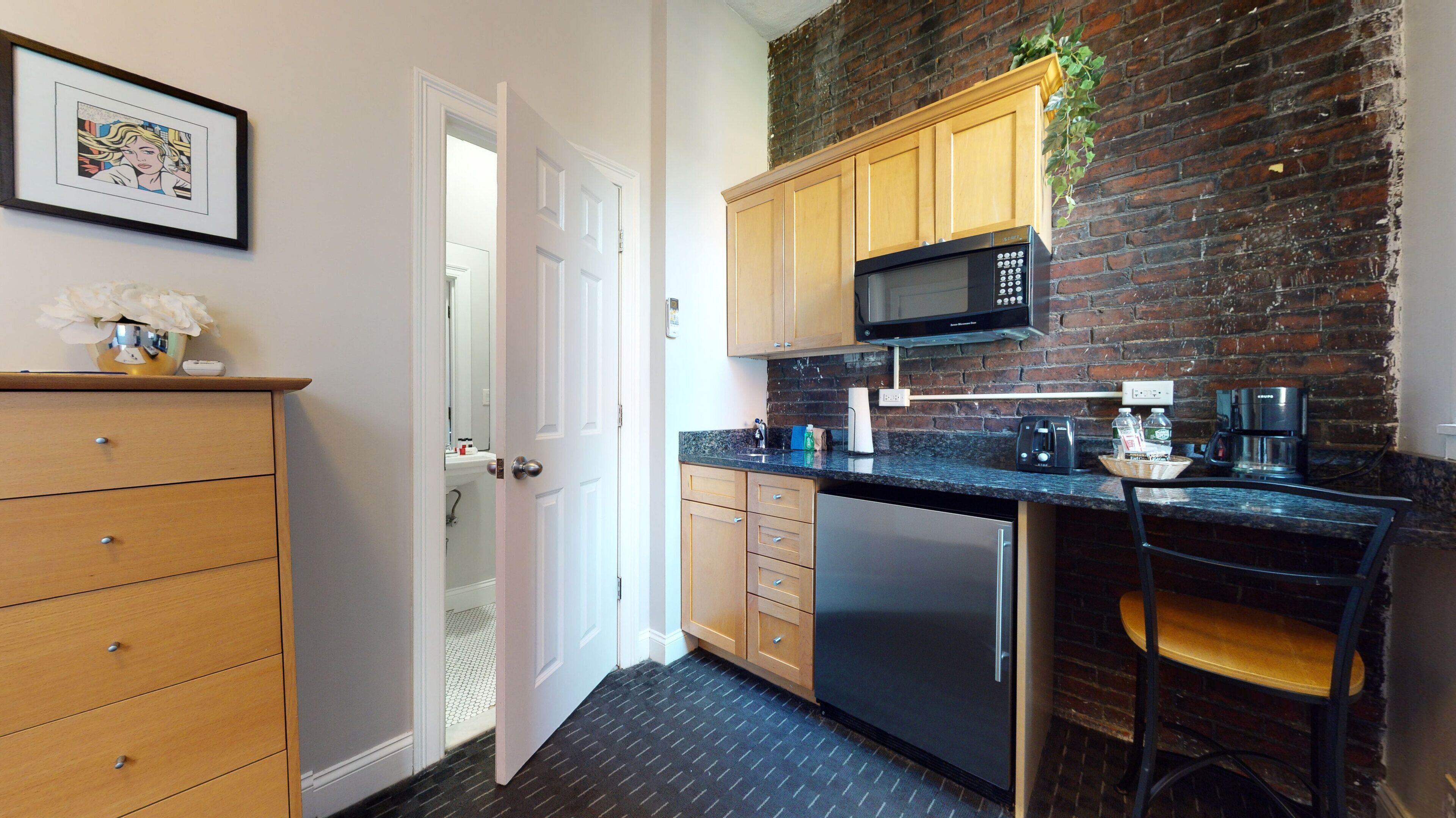 A compact kitchen with wooden cabinets, a black countertop, a stainless steel refrigerator, and a microwave.