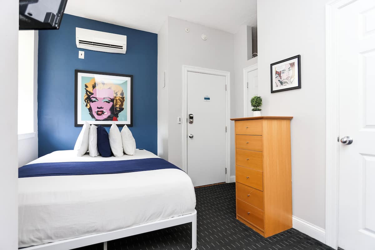 Habitación de hotel con cama, cómoda, puerta y un cuadro en la pared.