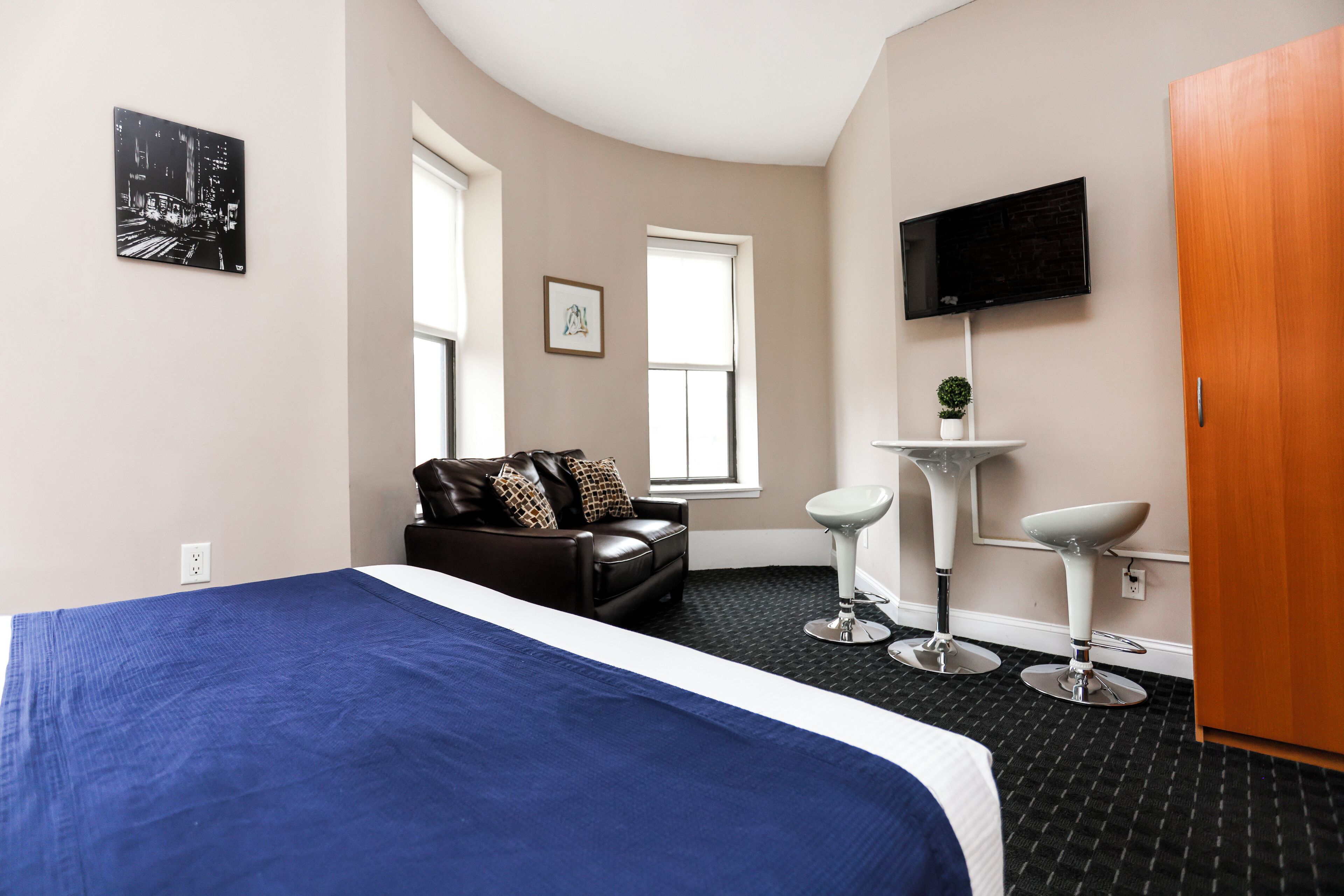 A hotel room with a bed, a sofa, a TV, a small table with a plant, and a bathroom with a sink and mirror.
