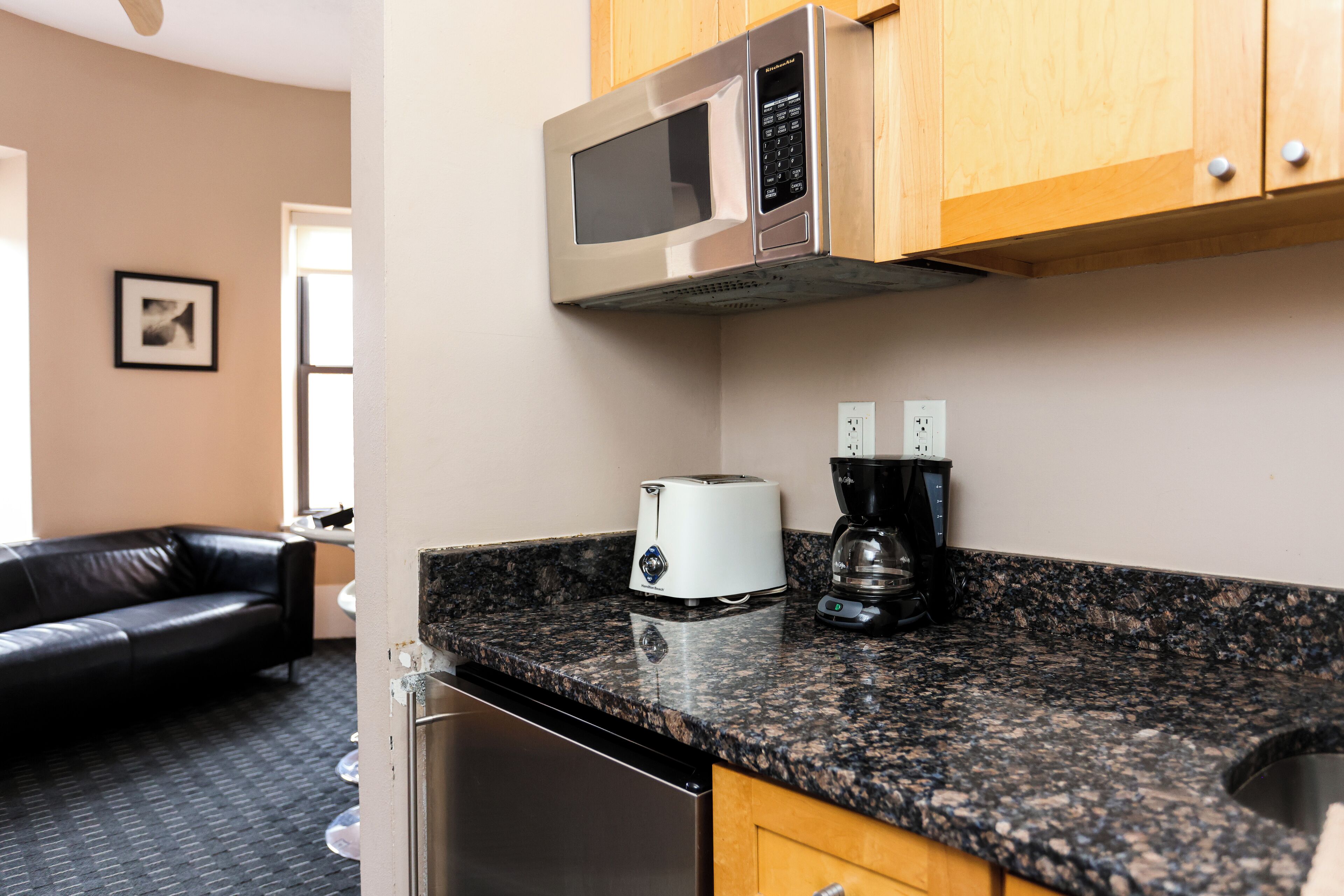 A kitchen with a microwave, toaster, and coffee maker on the counter, a dishwasher, and wooden cabinets.