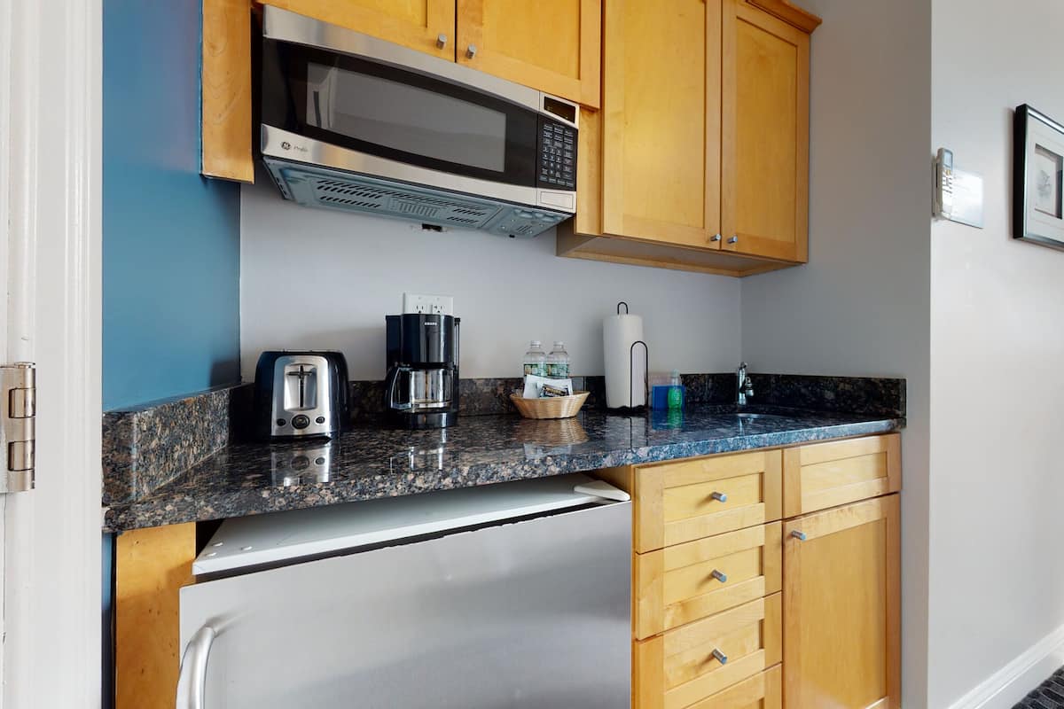 Una cocina compacta con armarios de madera, microondas integrado, tostadora, cafetera y lavamanos.