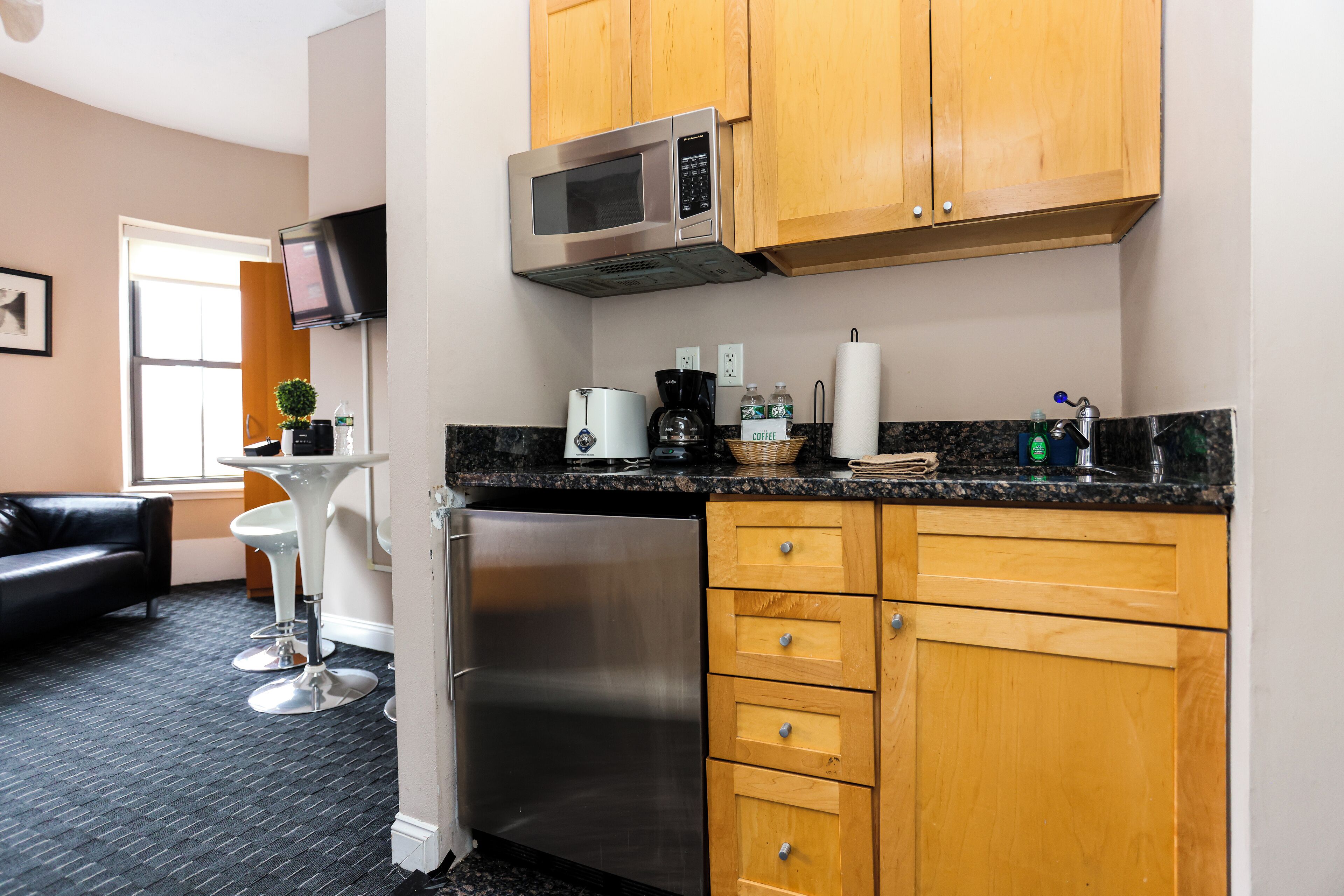A compact kitchen with wooden cabinets, a stainless steel refrigerator, a microwave, and a coffee maker.