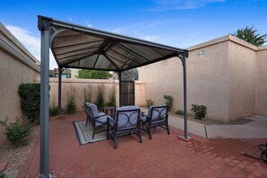 A covered patio with a table and chairs, a brick floor, and a beige wall.